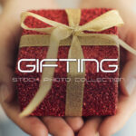 Christmas gifting stock photo collection featuring hands holding sparkly red gift box with gold ribbon bow and festive party decorations including red pom-pom garland and gold glitter circle banner against dark rustic wood background