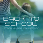 A high-quality stock photo from the BACK_TO_SCHOOL_Stock_Photo_11.jpg file featuring a young girl wearing a backpack walking on a sidewalk outside a brick school building under a leafy shade tree.